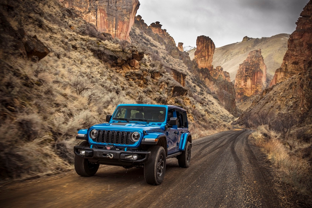 Front 3/4 view of the Jeep Wrangler 4-door hybrid driving on a dirt road.