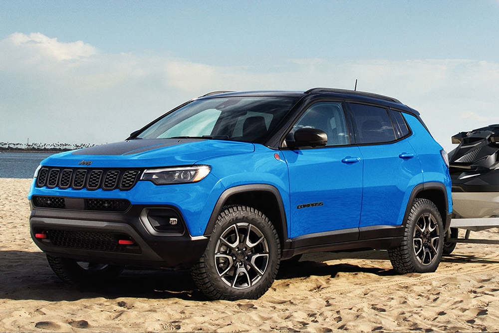 Vue 3/4 avant et latérale du Jeep Compass 2025 sur plage avec remorque et bateau